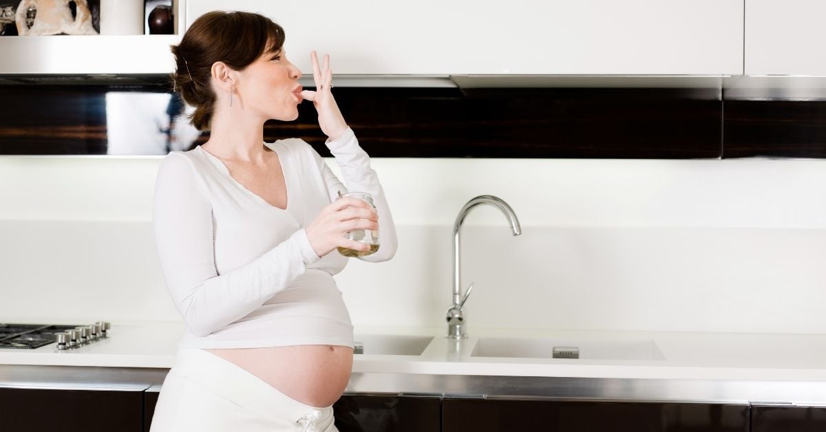 A pregnant woman holding a jar of raw honey and licking her finger