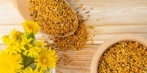 bee-pollen-benefits-natures-pharmacy Colourful granules of bee pollen spread on a wooden spoon and table